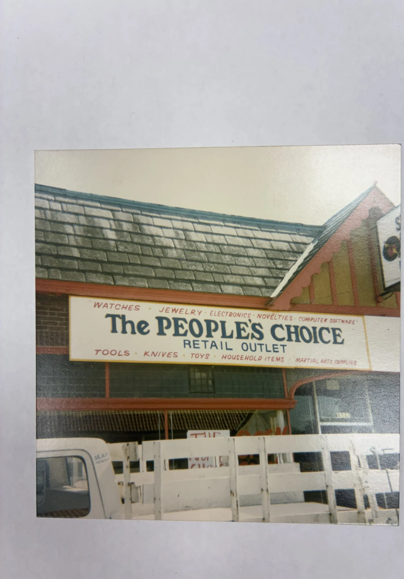 A 1983 color photograph of The People’s Choice Retail Outlet storefront sign in Waukegan, with the former Strawberry Fields sign visible at the upper right.