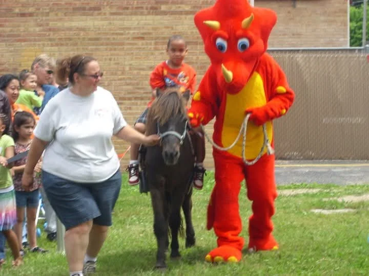 A boy rides a pony led alongside Rocky the mascot on the grass during Customer Appreciation Day at People’s Choice, 2011.