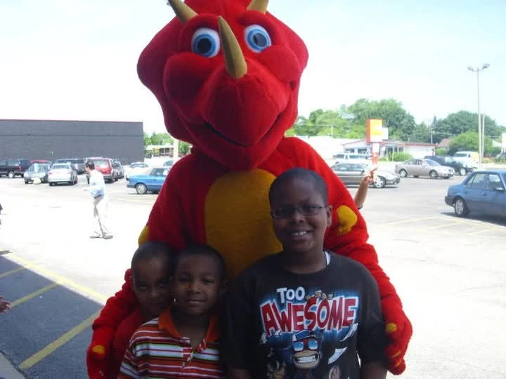 Three brothers pose with Rocky, the red People’s Choice dragon mascot, in the parking lot on Customer Appreciation Day, 2011.