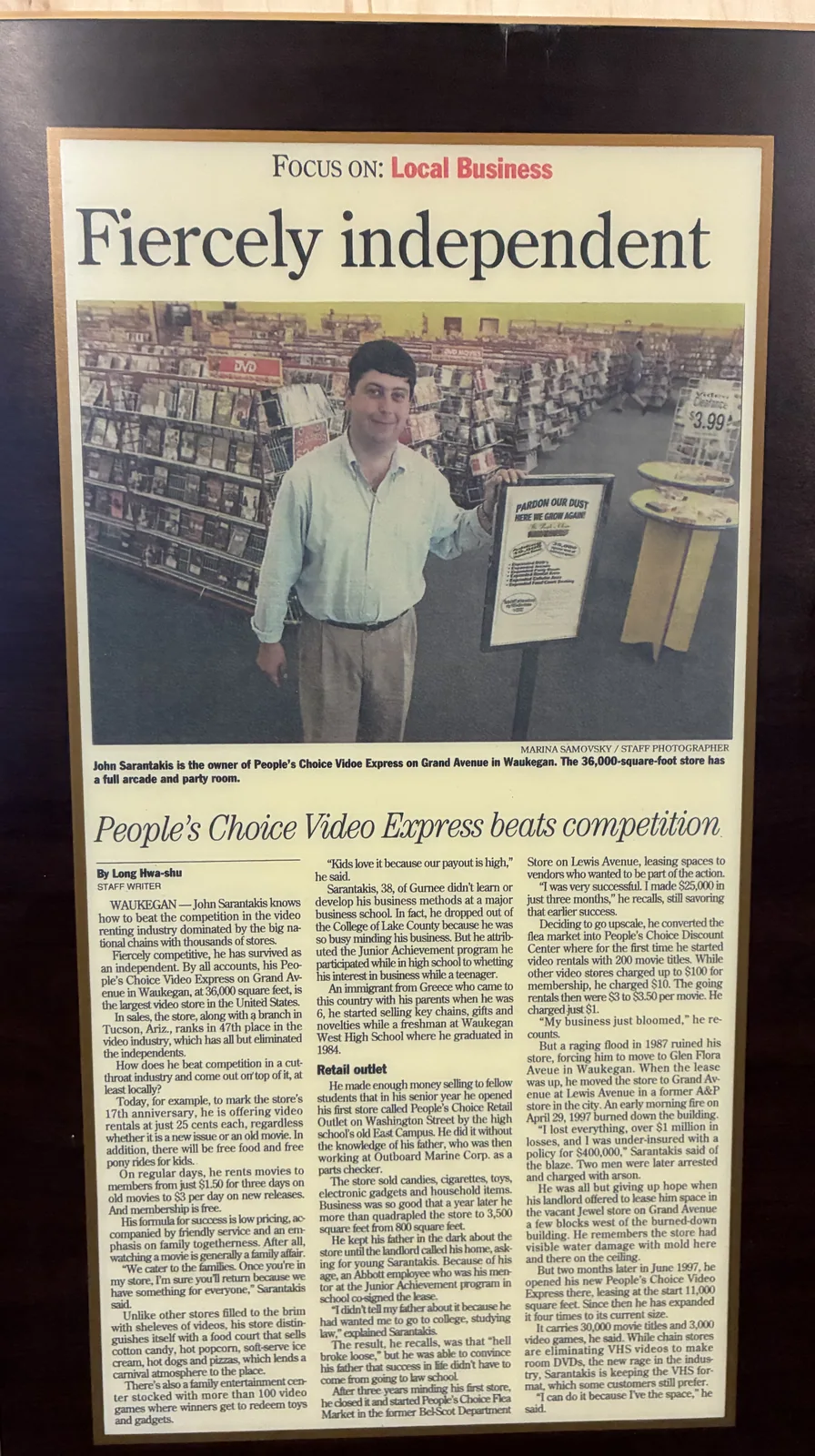 A framed local-business feature titled Fiercely independent, showing John Sarantakis inside People’s Choice Video Express on Grand Avenue.